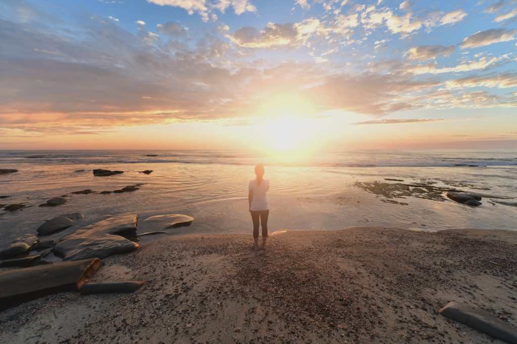 Person standing on beach at full sunrise.