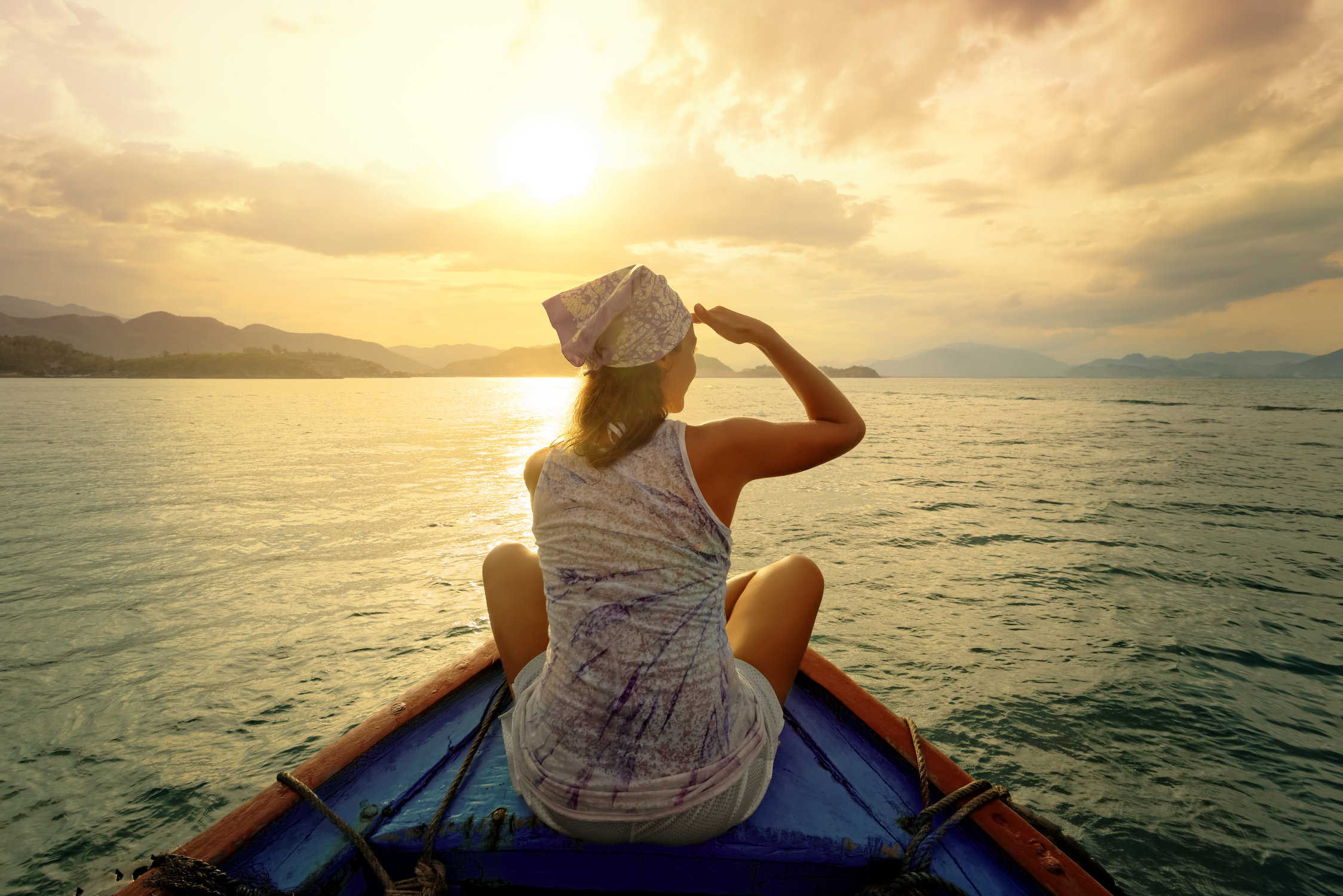 Woman at helm of boat looking towards the sunset in horizon